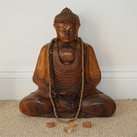Wooden Buddha in seated pose with mala beads and 3 small wooden hearts. This posture can be used for meditation. The Buddha and the hearts represent peaceful stillness in the body, mind and spirit and within the heart space.