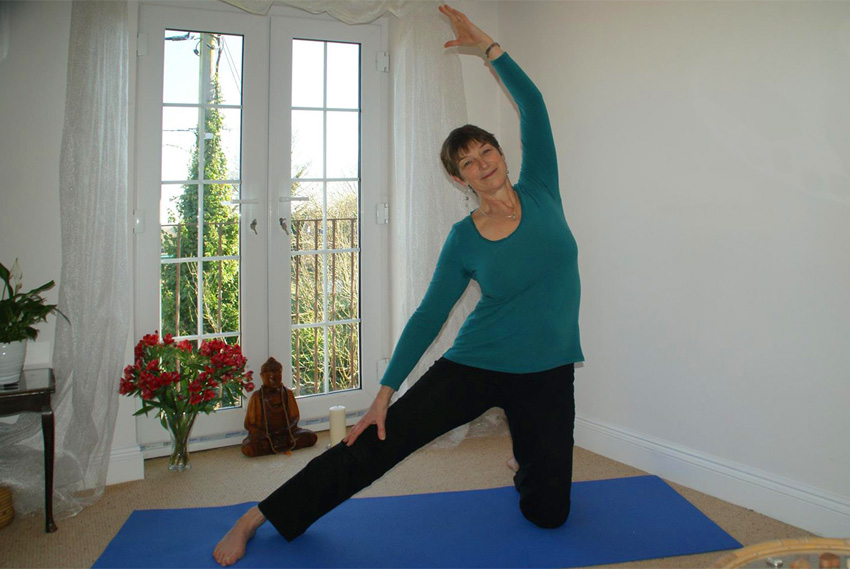 Cathie in her yoga space in 'gate' posture – half-high kneeling in side bend. Posture to open the side of the body and release shoulders.